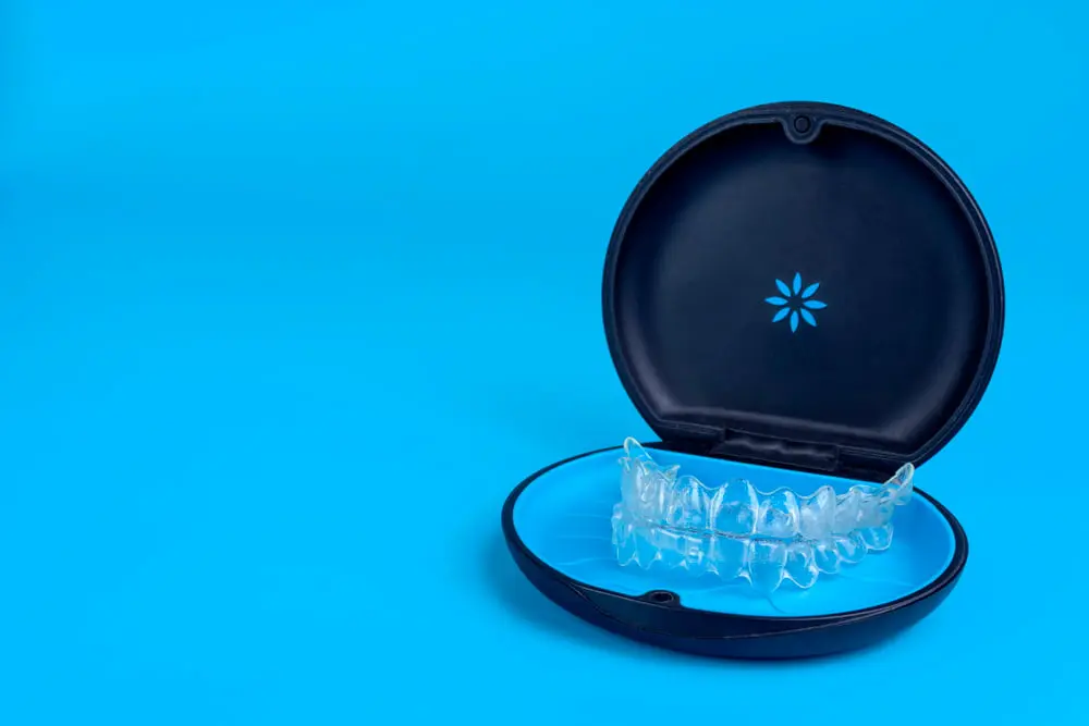 Black plastic case with transparent braces on blue background. Insivible removable retainers for orthodontic treatmen