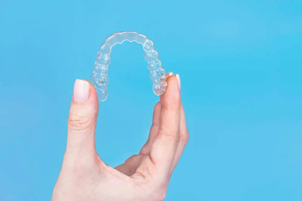 Hand holding removable invisible transparent aligner invisalign or plastic orthodontic braces retainer on blue background