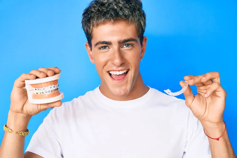 Young handsome man holding orthodontic smiling and laughing hard out loud because funny crazy joke