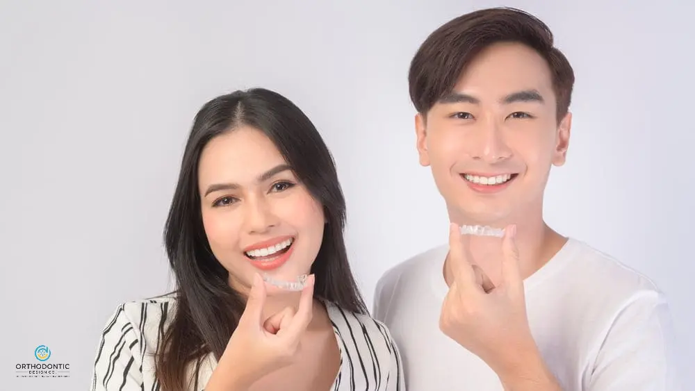 Two people smiling and holding clear dental aligners.