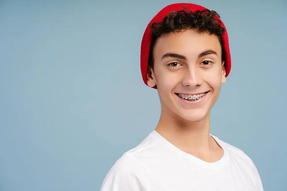 A smiling person with metal braces wears a red beanie and a white shirt against a blue background in Madison and Huntsville, AL A smiling person with metal braces wears a red beanie and a white shirt against a blue background in Madison and Huntsville, AL
