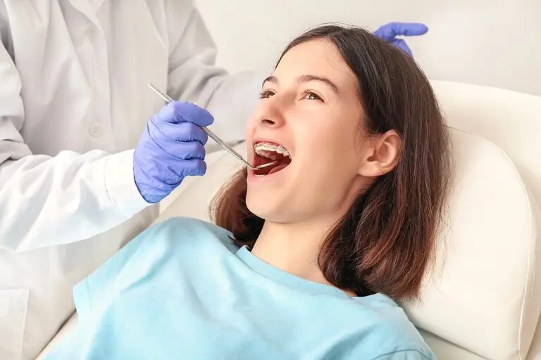 A young patient with braces sits in a dental chair with their mouth open while a gloved dentist examines their teeth to show How to Fix Overbite in Madison and Huntsville at Orthodontic Design Co. Orthodontics in Madison and Huntsville, AL.