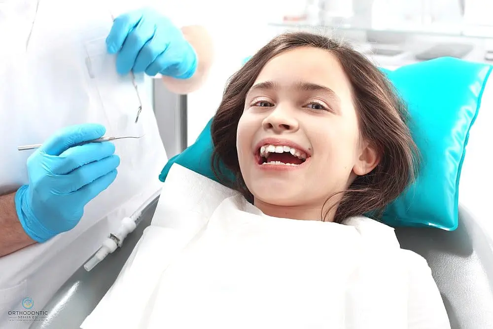 A young girl smiles in a dental chair as a dentist with blue gloves discusses how to fix overbite in Madison and Huntsville, AL at Orthodontic Design Co. Orthodontics.