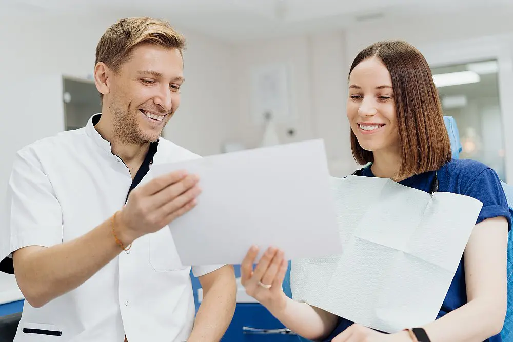At a welcoming dental office, a dentist and patient smile while reviewing an x-ray and discussing affordable Invisalign options at Orthodontic Design Co. Orthodontics in Madison and Huntsville, AL.