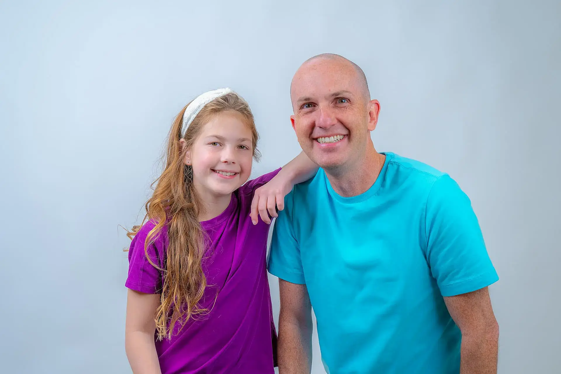 Dr. Adam Reynolds in a blue shirt and a girl in a purple shirt, both proudly displaying their clear aligners, pose together against a plain background—showcasing Orthodontic Design Co. Orthodontics in Madison and Huntsville, AL. Dr. Adam Reynolds in a blue shirt and a girl in a purple shirt, both proudly displaying their clear aligners, pose together against a plain background—showcasing Orthodontic Design Co. Orthodontics in Madison and Huntsville, AL.