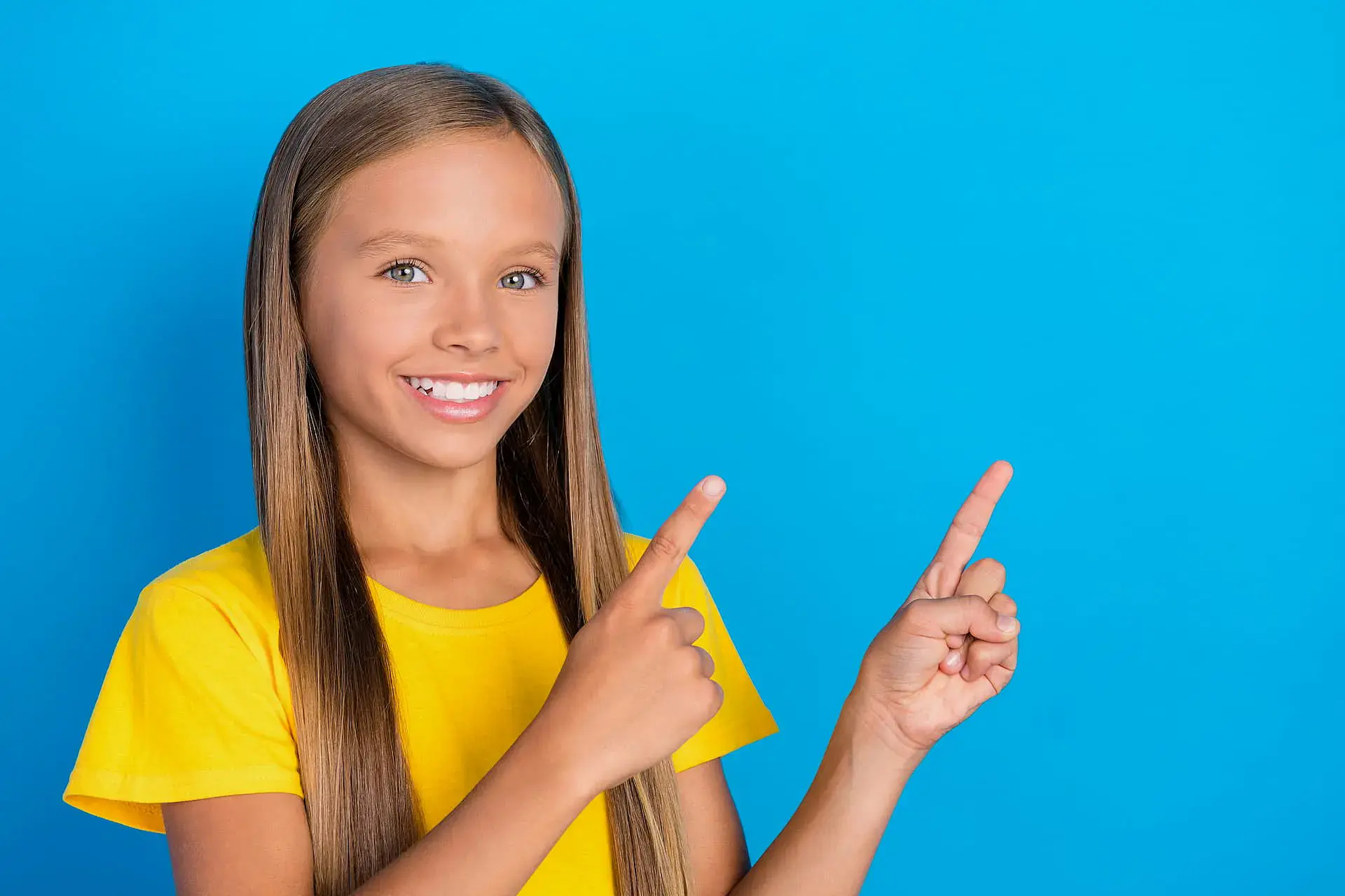 A smiling girl with long straight hair and a yellow shirt points up to the right against a blue background, promoting Orthodontic Design Co. Orthodontics as a Children’s Orthodontist in Madison and Huntsville, AL.