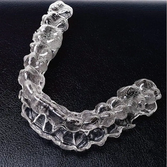 Displayed on a black surface, a clear Invisalign aligner reveals detailed teeth impressions used by Orthodontist at Orthodontic Design Co. Orthodontics in Huntsville, AL.