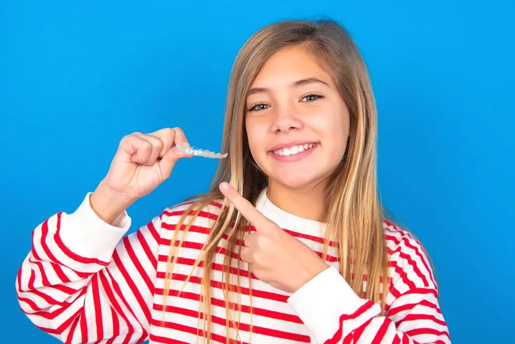 A teen points to Invisalign aligners against a blue background, Orthodontist and Orthodontics in Madison and Huntsville, AL.