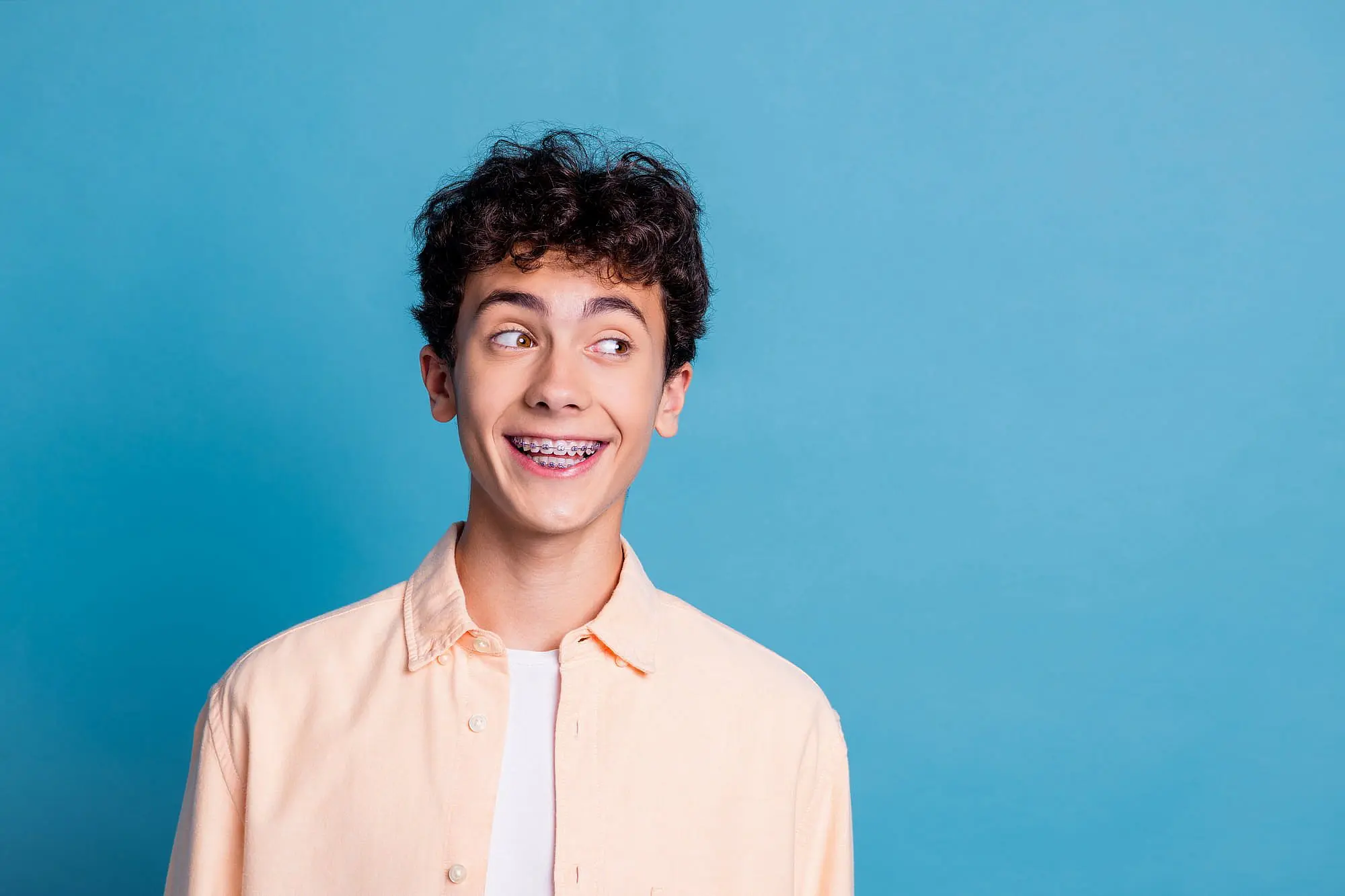 A teenage boy with curly dark hair and braces as a pateint of Orthodontic Design Co. Orthodontics in Madison and Huntsville, AL.