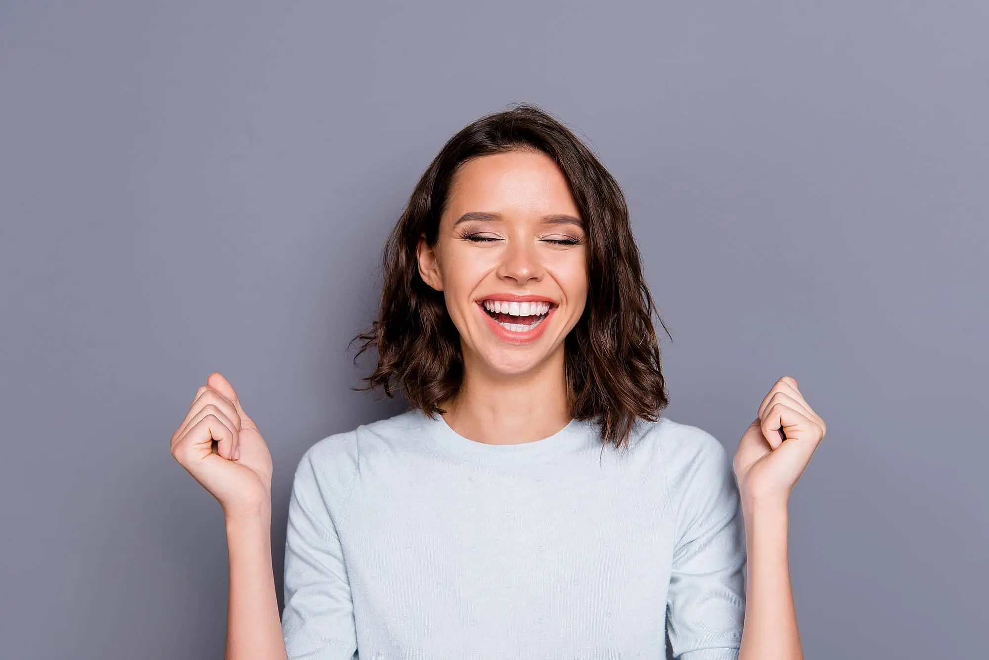 A young woman smiles with happy eyes closed and clenched fists, representing Orthodontic Design Co. Orthodontics in Madison and Huntsville, AL.
