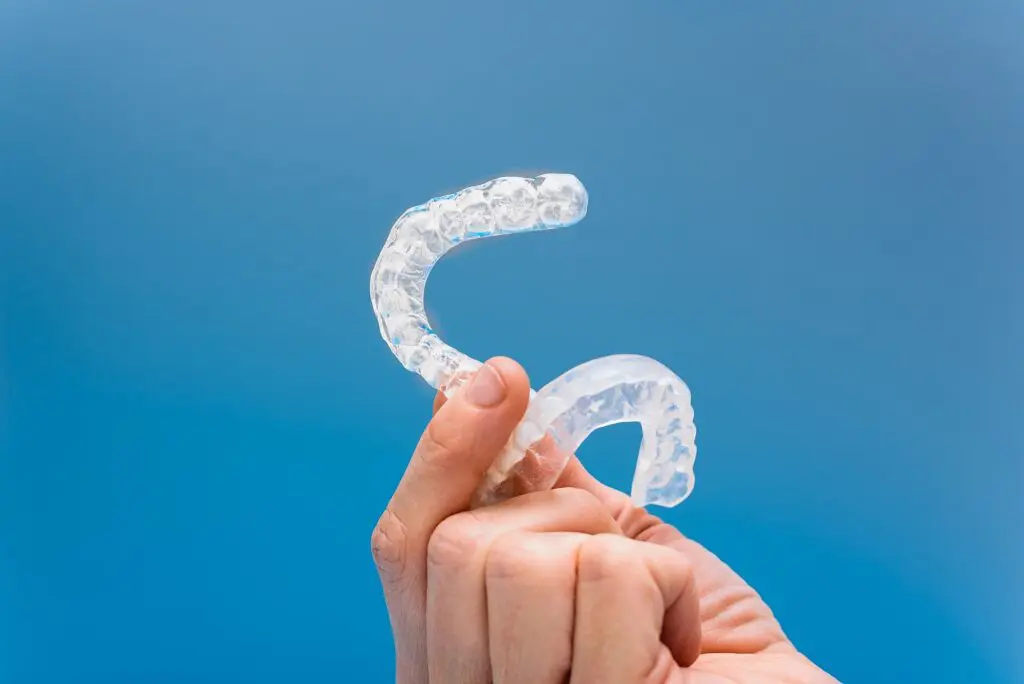 Two clear dental aligners are held by a hand with a blue background for Orthodontic Design Co. Orthodontics in Madison and Huntsville, AL.