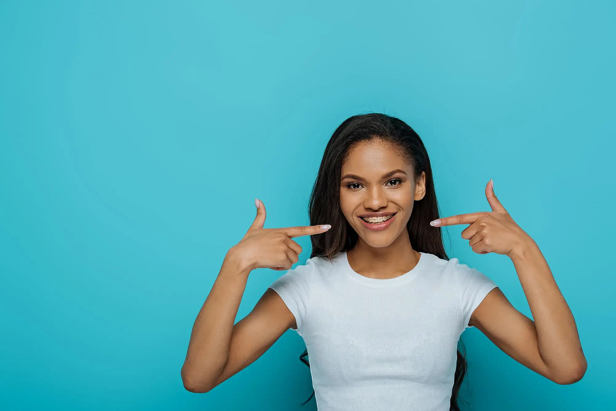 A young woman points to her braces, smiling, representing Orthodontic Design Co. Orthodontics in Madison and Huntsville, AL.