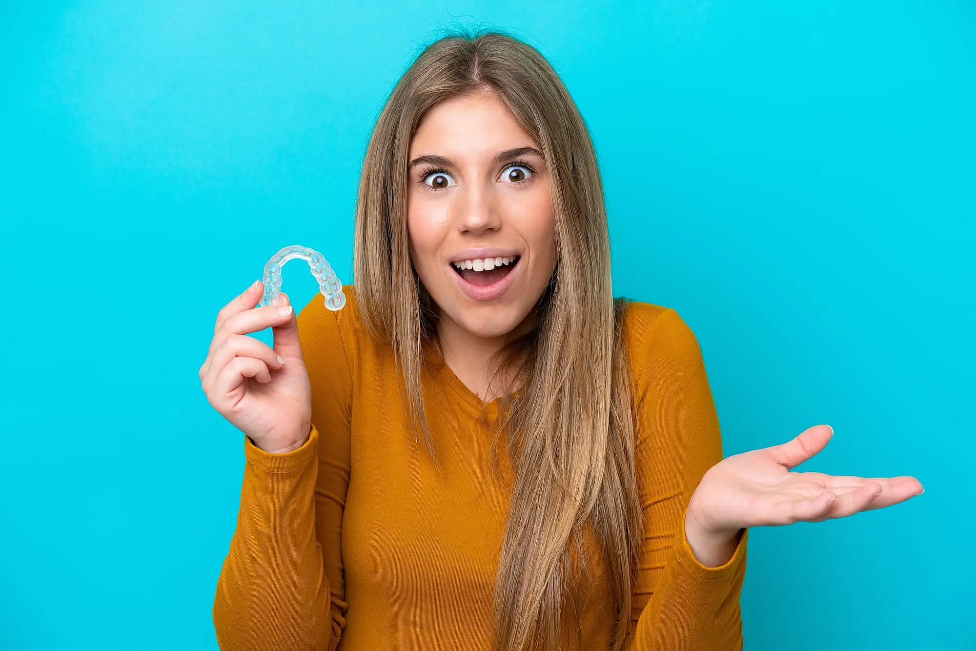A young woman holds a clear dental aligner, promoting Orthodontic Design Co. Orthodontics in Madison and Huntsville, AL.