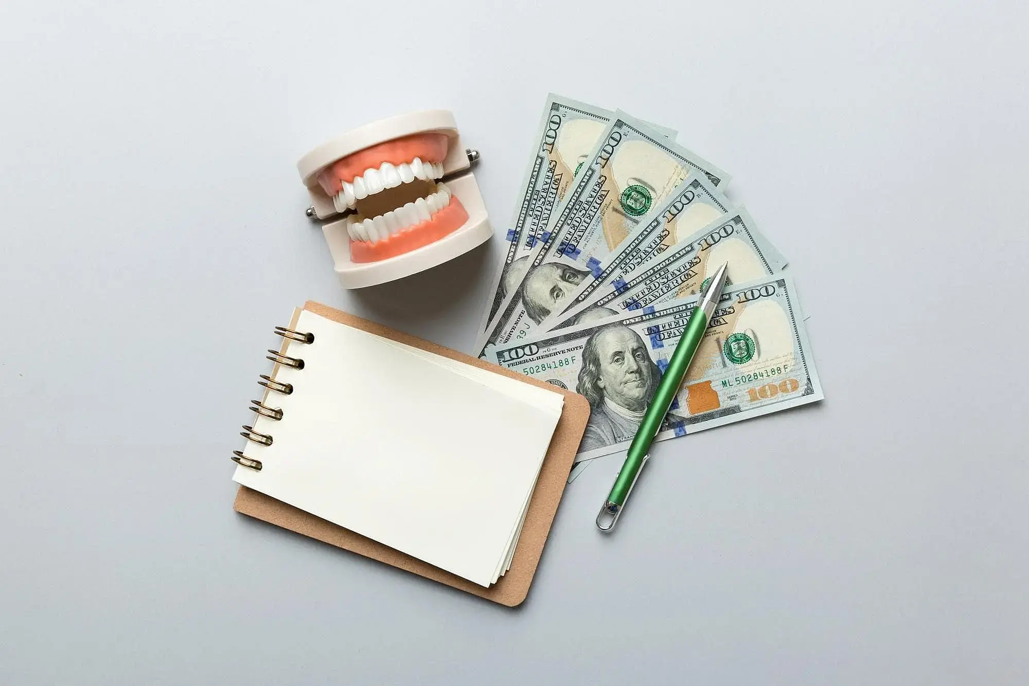 On a white surface, a dental model, $100 bills, notebook, and green pen highlight Invisalign payment at Orthodontic Design Co. Orthodontics in Madison and Huntsville, AL. On a white surface, a dental model, $100 bills, notebook, and green pen highlight Invisalign payment at Orthodontic Design Co. Orthodontics in Madison and Huntsville, AL.