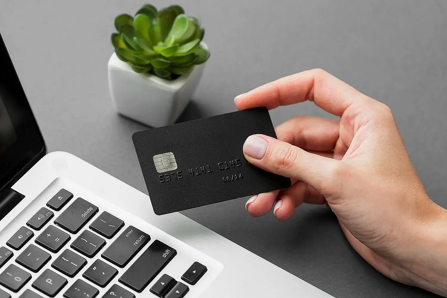 A hand holds a black credit card near a laptop keyboard, show Invisalign payment at Orthodontic Design Co. Orthodontics in Madison and Huntsville, AL. A hand holds a black credit card near a laptop keyboard, show Invisalign payment at Orthodontic Design Co. Orthodontics in Madison and Huntsville, AL.