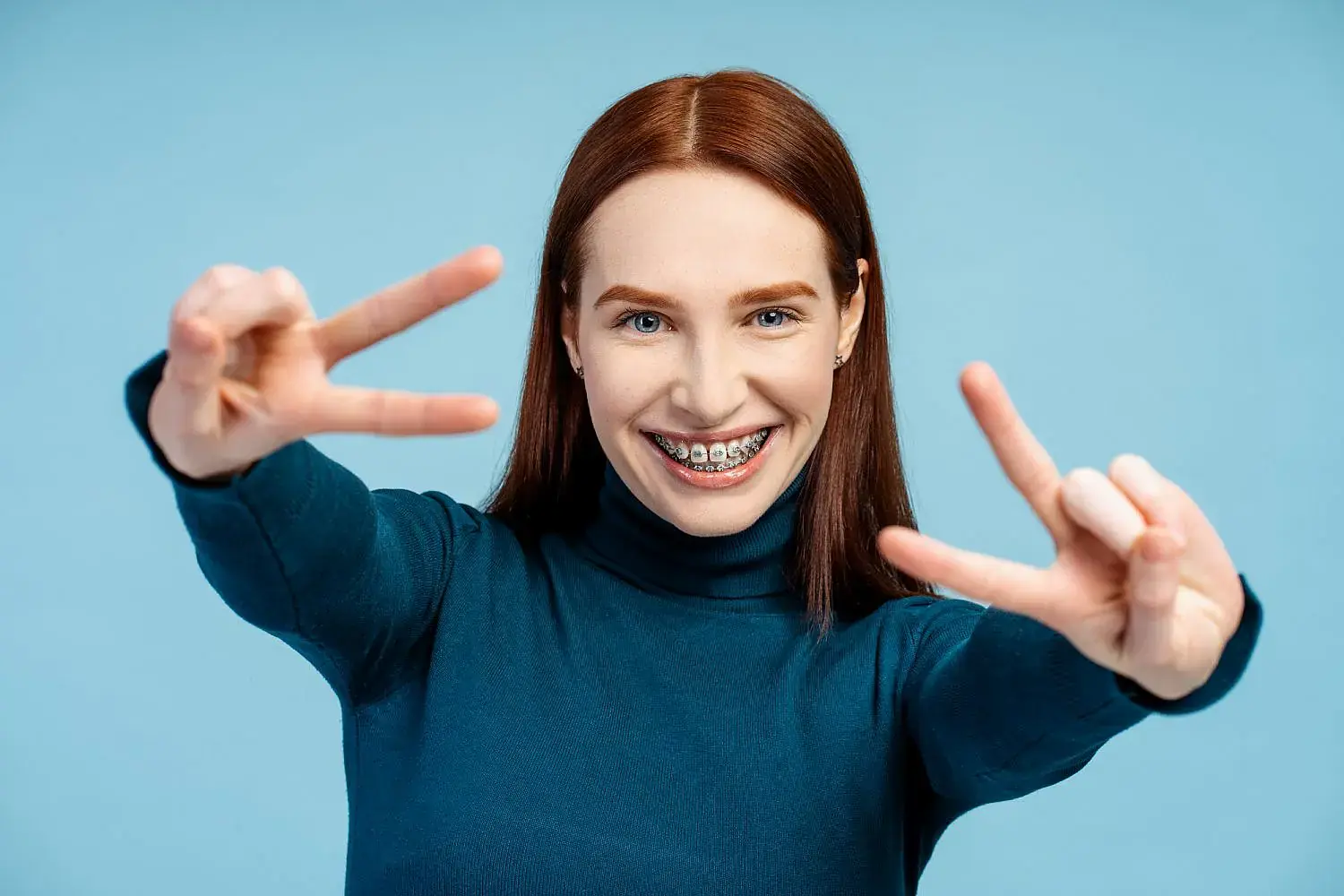 Smiling young woman with braces flashes peace signs after considering Invisalign vs Braces at Orthodontic Design Co. Orthodontics in Madison and Huntsville, AL. Smiling young woman with braces flashes peace signs after considering Invisalign vs Braces at Orthodontic Design Co. Orthodontics in Madison and Huntsville, AL.