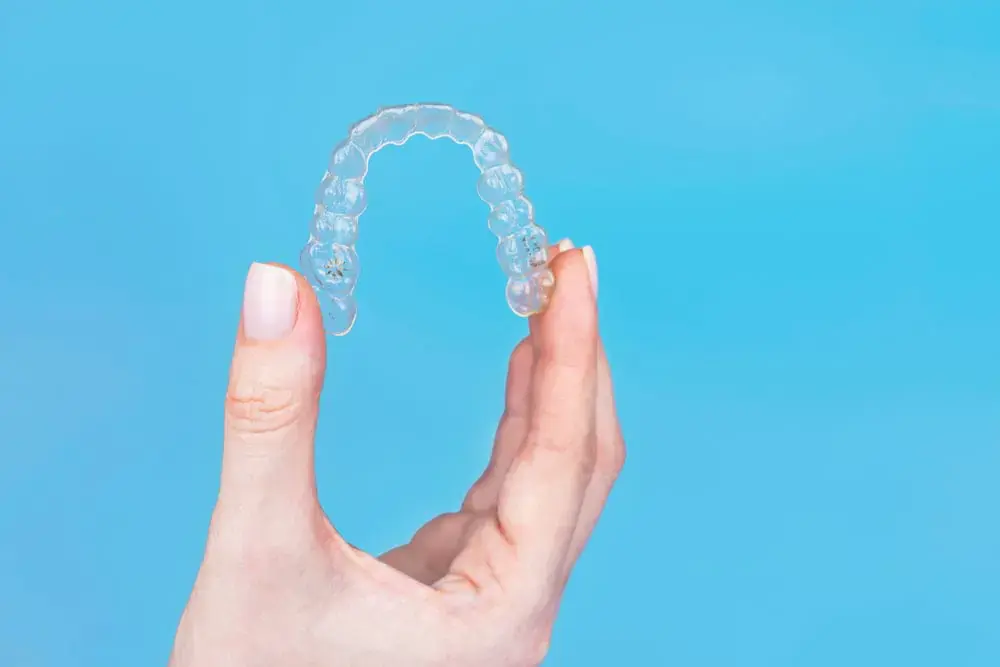 An Invisalign aligner is held by a manicured hand against blue, representing Orthodontic Design Co. Orthodontics in Huntsville, AL. An Invisalign aligner is held by a manicured hand against blue, representing Orthodontic Design Co. Orthodontics in Huntsville, AL.