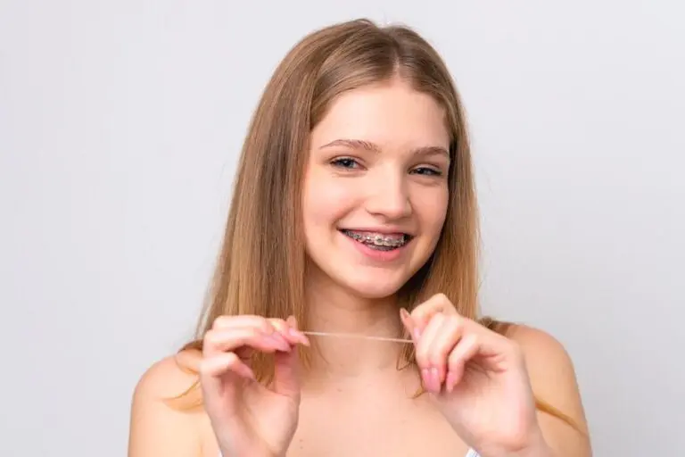 Smiling teen with long blonde hair and braces shows dental floss; Orthodontic Design Co. Orthodontics in Madison and Huntsville, AL - How to Floss with Braces in Madison and Huntsville, AL.