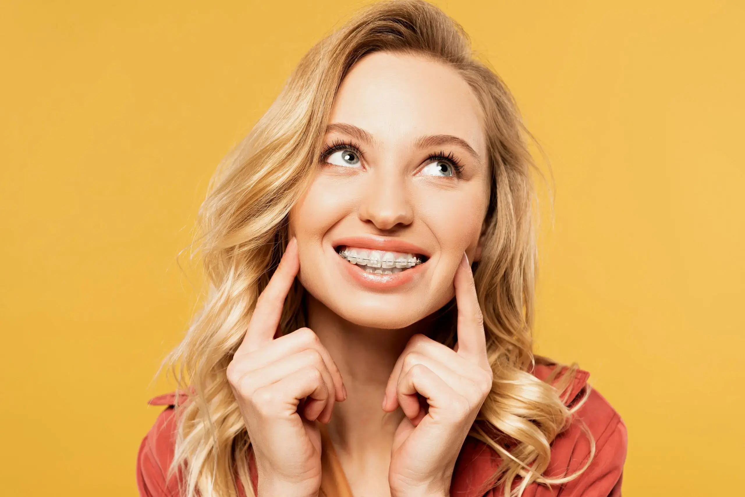 A young woman with blonde hair smiles and points to her metal braces, promoting Orthodontic Design Co. Orthodontics in Madison and Huntsville, AL, against a yellow background. A young woman with blonde hair smiles and points to her metal braces, promoting Orthodontic Design Co. Orthodontics in Madison and Huntsville, AL, against a yellow background.