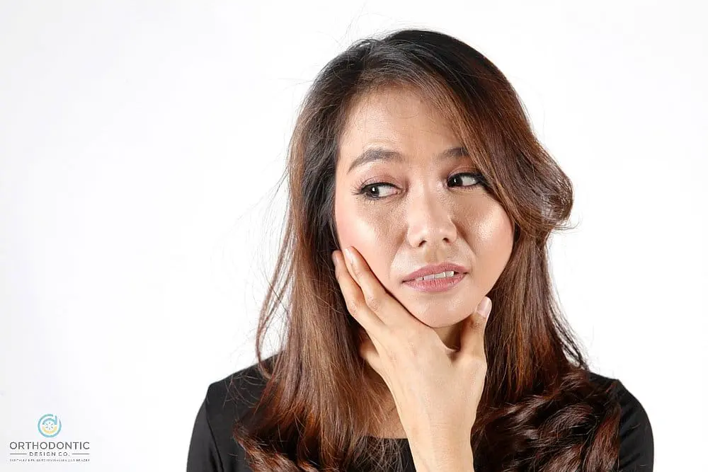 A woman with long brown hair holds her jaw in discomfort, representing Orthodontic Design Co. Orthodontics in Madison and Huntsville, AL - TMJ Treatment in Madison and Huntsville, AL
