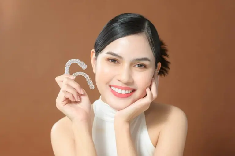 Smiling woman holds two clear dental aligners, with Orthodontic Design Co. Orthodontics in Madison and Huntsville, AL, shown - How Does Invisalign Work in Madison and Huntsville, AL