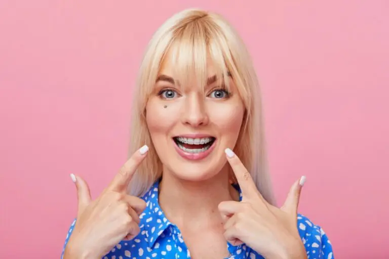A smiling blonde woman points to her dental braces, promoting Orthodontic Design Co. Orthodontics in Madison and Huntsville, AL - Clear Braces vs Metal Braces in Madison and Huntsville, AL
