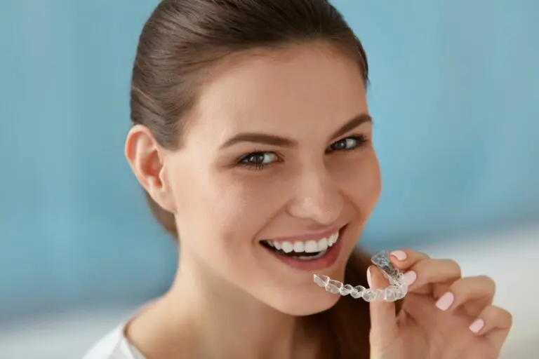 A woman smiles, holding a clear aligner near her mouth; Orthodontic Design Co. Orthodontics in Madison and Huntsville, AL - How Long Does Invisalign Take in Madison and Huntsville, AL
